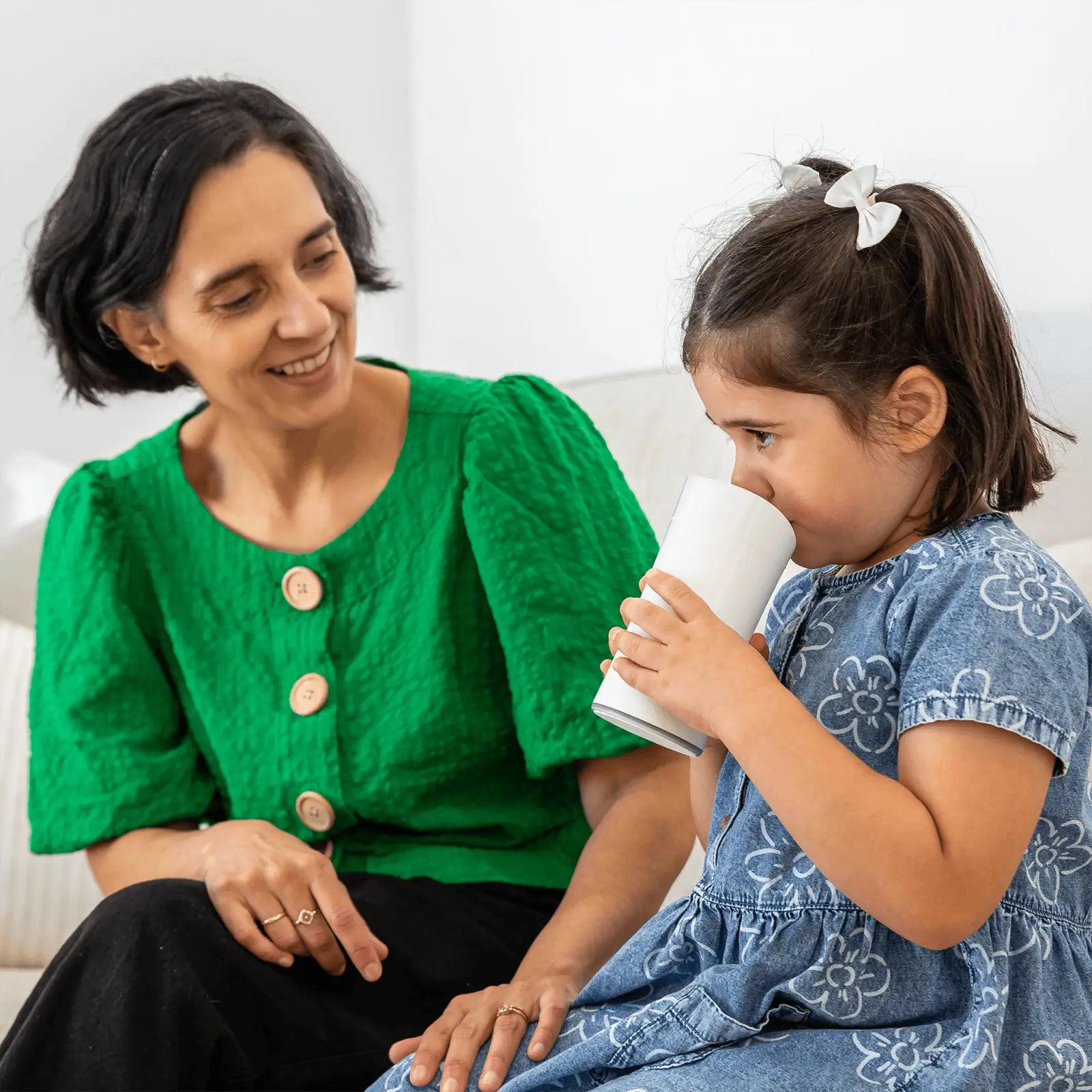 Parent sitting next to child while child drinks from the Earflo device like a sippy cup